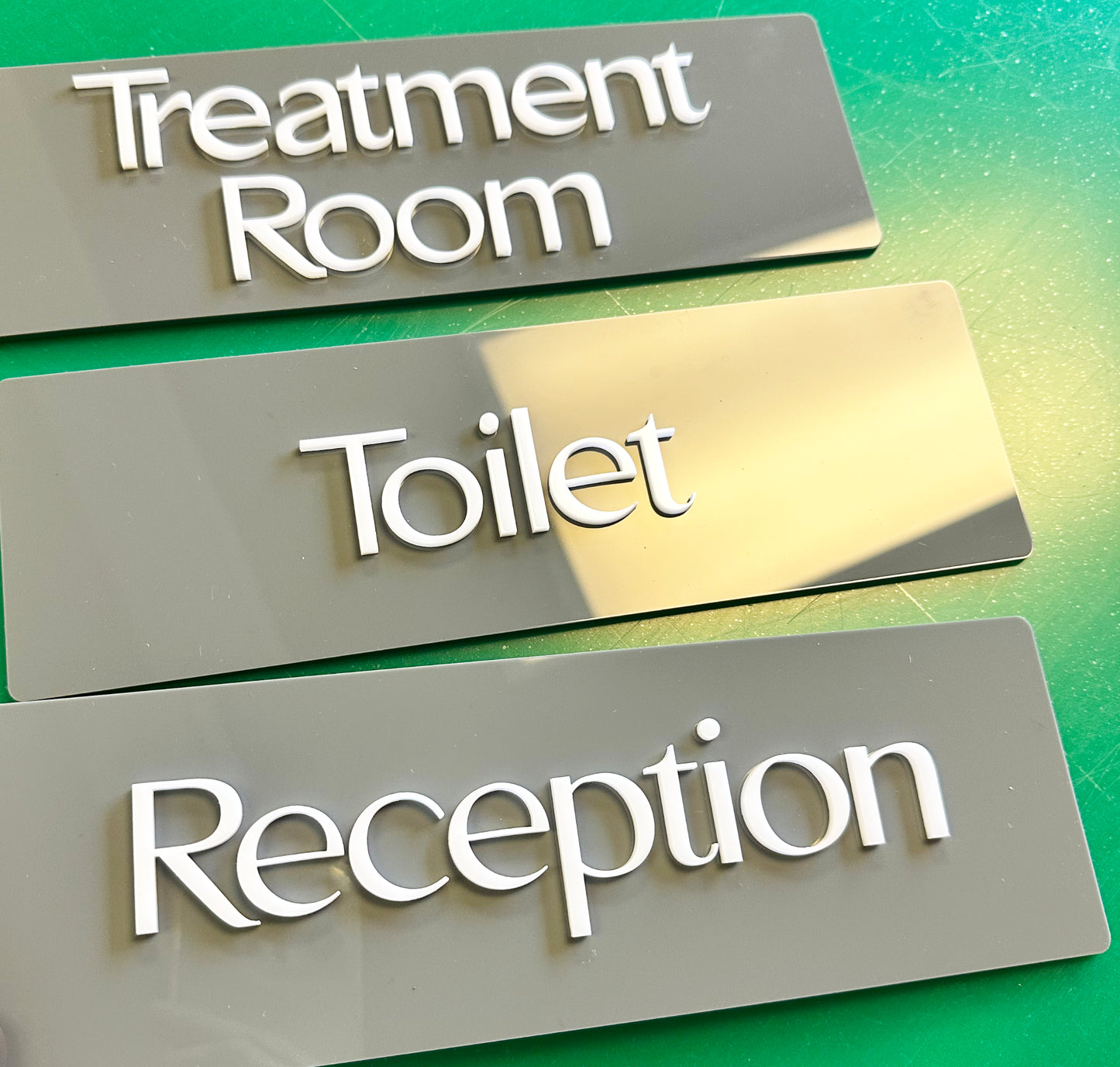 Acrylic nameplates labeled 'Treatment Room', 'Toilet', and 'Reception' on a green gradient background.