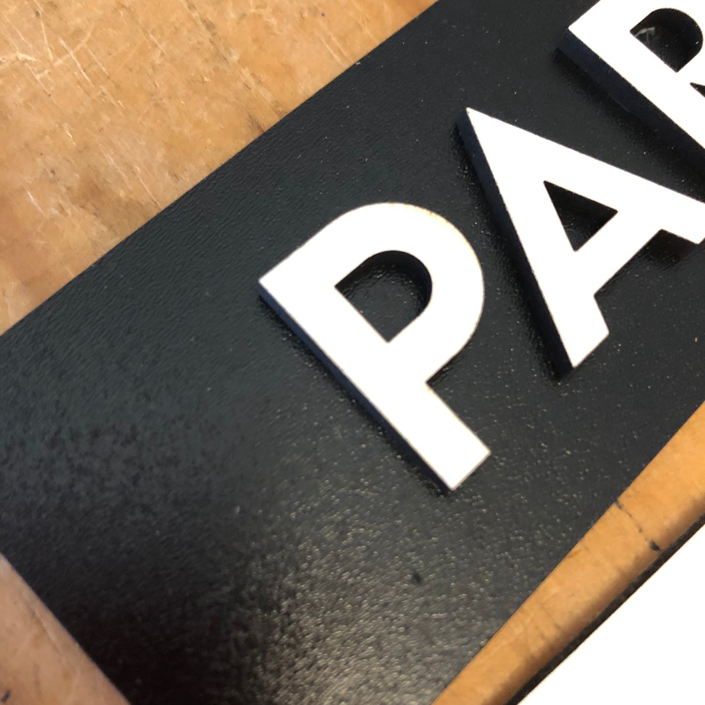 Close-up of a black sign with white letters on a wooden surface
