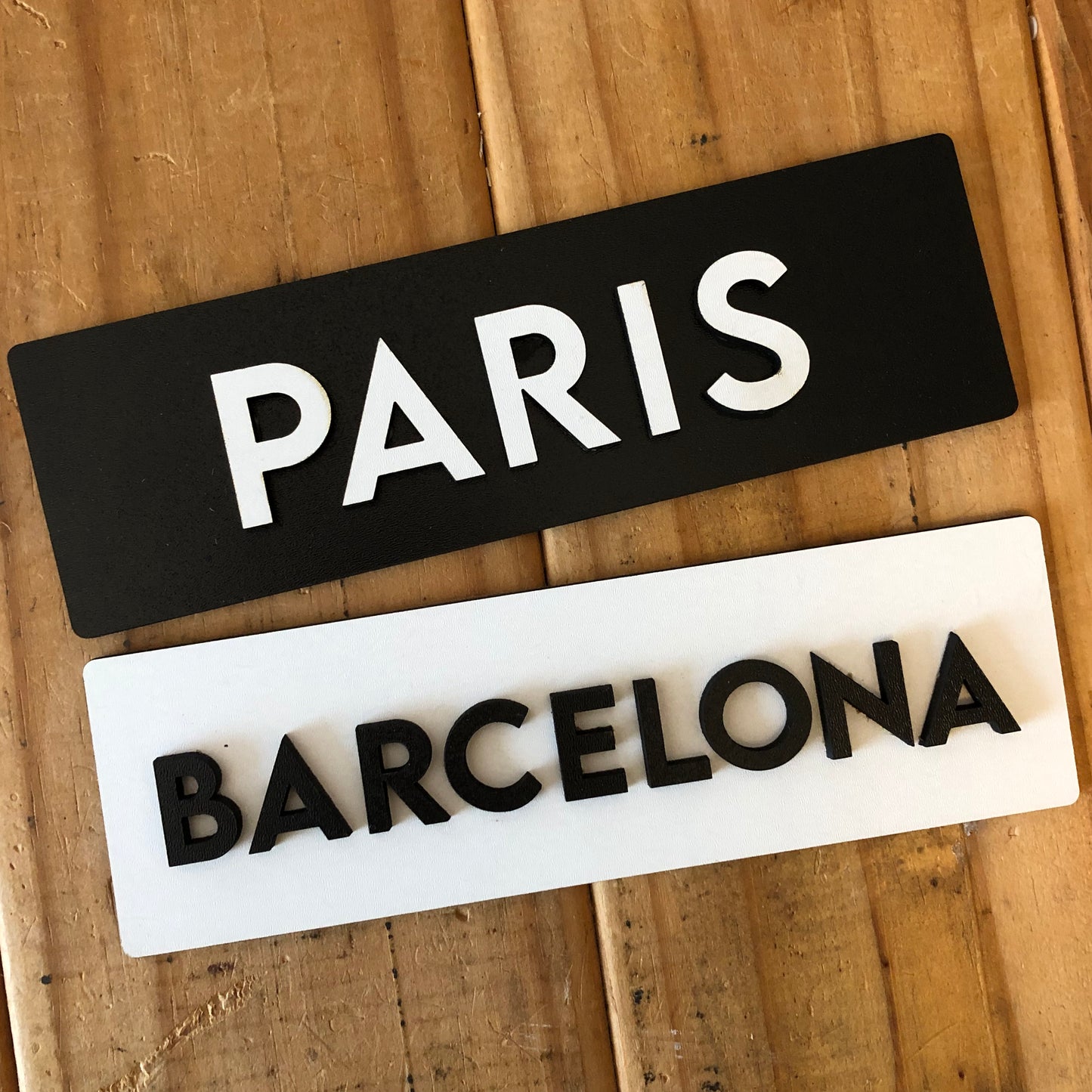 Two decorative signs with 'PARIS' and 'BARCELONA' text on a wooden surface.