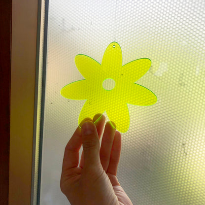 Hand holding a yellow flower-shaped object against a glass surface