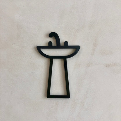 A black acrylic bathroom door sign with a stylized design, featuring a silhouette of a sink on a square base with a curved handle.