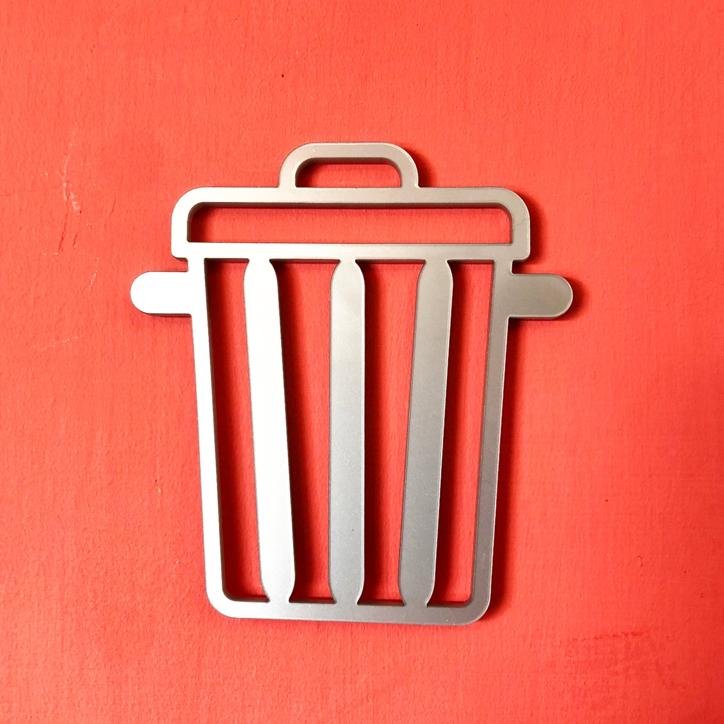 Metal trash bin door sign in silver on a coral background