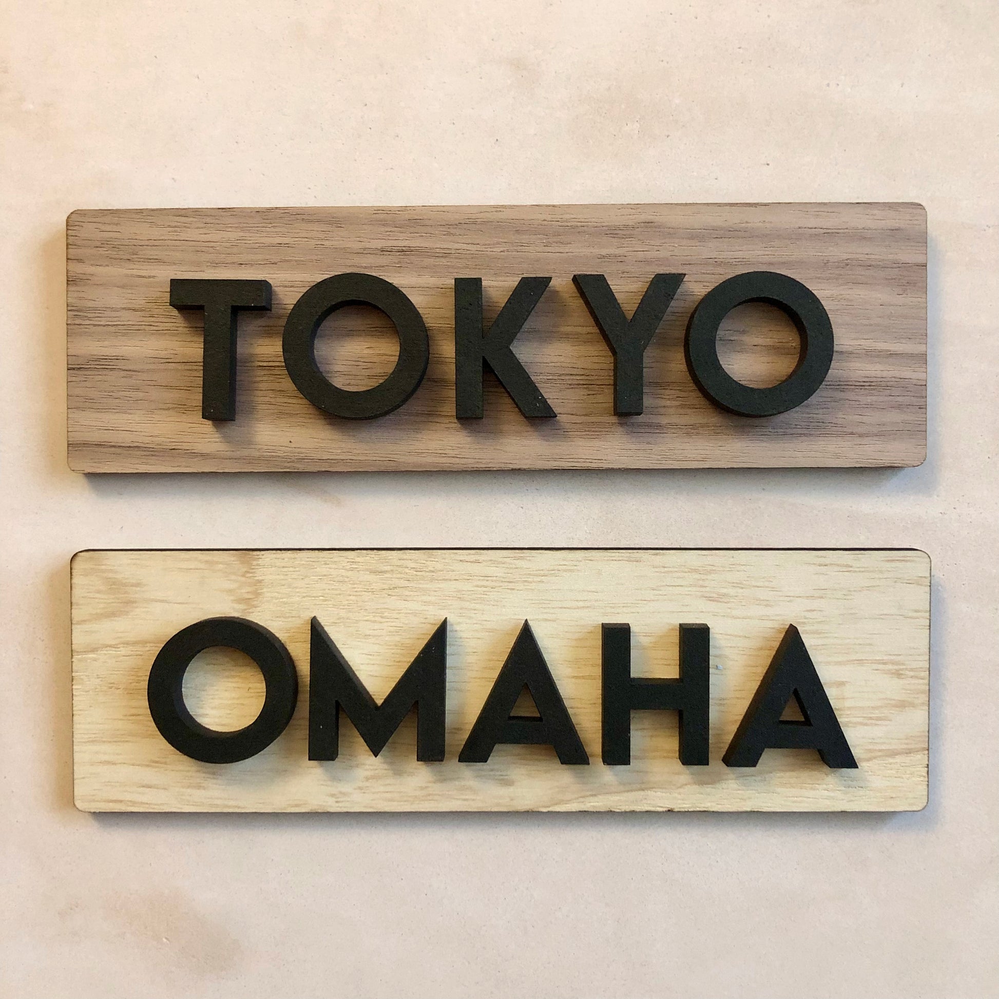 Two wooden signs with 'TOKYO' and 'OMAHA' text on a beige background