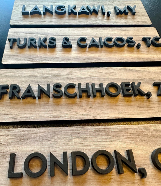 Wooden signs with embossed city names on a dark surface